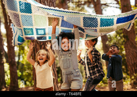 Vier Kinder im Park tanzen unter eine Picknickdecke. Gruppe von Kindern Spaß zusammen in den Park. Stockfoto