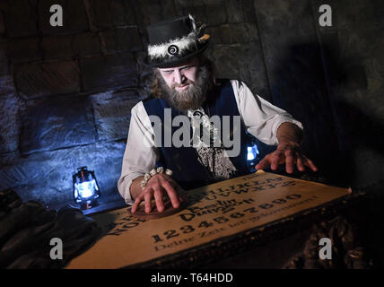 Berlin, Deutschland. 24 Apr, 2019. Der Schauspieler Alex van Ric (als Medium) mit einem Ouija Brett an der Berliner Dungeon. Die show éance - Haben Sie Ihr das Gefühl auch?" geht es um ein Medium, das versucht, den Geist einer Frau während einer Nekromantie zu zaubern. Quelle: Britta Pedersen/dpa-Zentralbild/ZB/dpa/Alamy leben Nachrichten Stockfoto