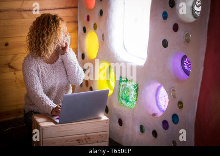 Alternative zu Hause oder im Büro Arbeitsplatz für junge Lockige wunderschöne Frau auf dem Boden sitzend arbeiten an einem Laptop aus dem Fenster zu schauen - Technologie Stockfoto