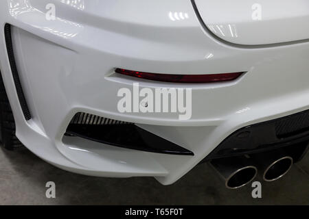 Der hintere Stoßfänger des eine getunte Auto ist weiß mit einem Doppel Auspuff Düse, ein diffuser und einem roten Reflektor in einem Fahrzeug tuning Werkstatt. Auto Service indust Stockfoto