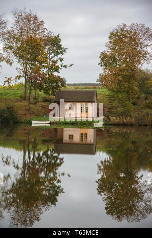 See mit Reflexion von Bäumen und einem kleinen Bootfahren Hütte im See, die perfekt ist, ohne einen einzigen Welligkeit stören das Wasser ruhig widerspiegelt Stockfoto