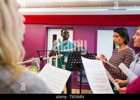 Männliche Leiter der führenden Frauen Chor mit Noten singen in Music Recording Studio Stockfoto