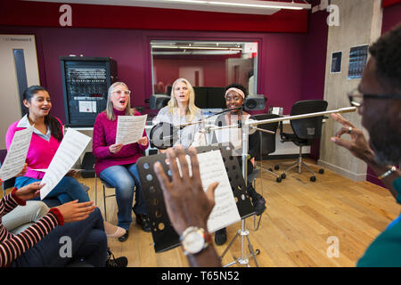 Männliche Leiter der führenden Frauen Chor mit Noten singen in Music Recording Studio Stockfoto