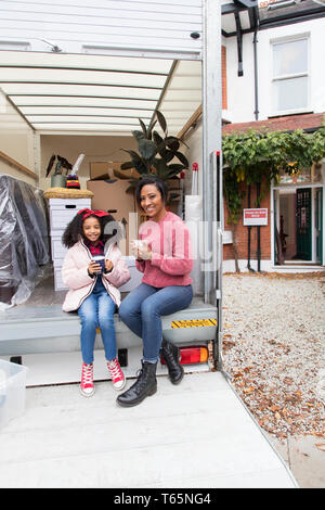 Portrait glückliche Mutter und Tochter trinkt Tee, eine Pause an der Rückseite des Moving van außerhalb neues Haus Stockfoto