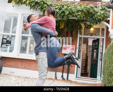 Glücklich, aufgeregt Paar umarmen und Feiern außerhalb neues Haus Stockfoto