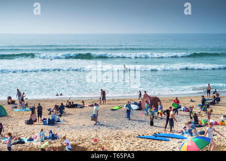 Urlauber genießen die Sonne auf einer belebten Fistral Beach in Newquay in Cornwall. Stockfoto