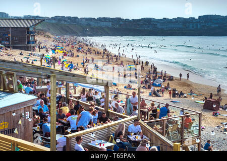 Urlauber genießen die Sonne an einem besetzten Fistral Beach in Newquay in Cornwall. Stockfoto