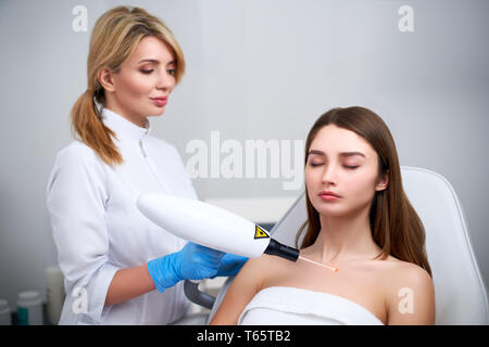 Laser mole Ausbau auf einer Frau, die in der Brust in einem Schönheitssalon. Hardware Kosmetologie. Hübsche Blondine Kosmetikerin Arzt entfernen Muttermal oder Muttermale mit Laser Stockfoto