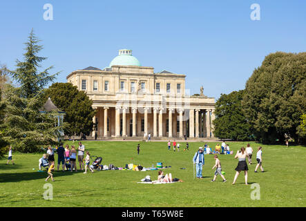 Cheltenham Pittville Pump Room mit Menschen bei einem Picknick und spielende Kinder Pittville Park, Cheltenham Spa Gloucestershire, England, UK, GB, Europa Stockfoto