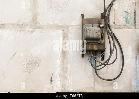 Alten rostigen ungepflegt elektrische Abschirmung mit einem Schalter an der Wand eines industriellen Gebäude aus Beton Bausteine mit geschmolzene Drähte festsitzen heraus Stockfoto