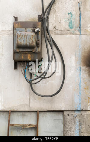 Alten rostigen ungepflegt elektrische Abschirmung mit einem Schalter an der Wand eines industriellen Gebäude aus Beton Bausteine mit geschmolzene Drähte festsitzen heraus Stockfoto