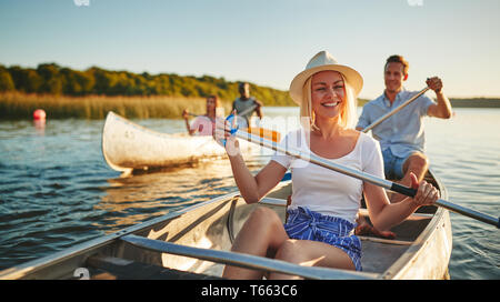 Junge Frau lacht beim paddeln im Kanu auf einem malerischen See mit einer Gruppe von Freunden an einem sonnigen Nachmittag Stockfoto