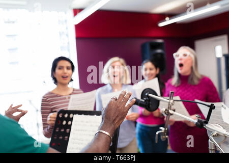 Männliche Leiter der führenden Frauen Chor mit Noten singen in Music Recording Studio Stockfoto