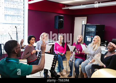 Männliche Leiter der führenden Frauen Chor mit Noten singen in Music Recording Studio Stockfoto