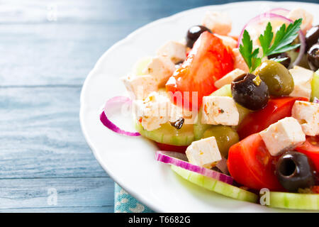 Frischen griechischen Salat mit Tomaten, Gurken, Zwiebeln, Schafskäse und Oliven auf einem blauen Holztisch Stockfoto