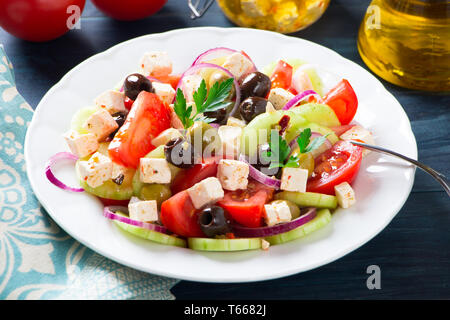 Frischen griechischen Salat mit Tomaten, Gurken, Zwiebeln, Schafskäse und Oliven auf einem blauen Holztisch Stockfoto