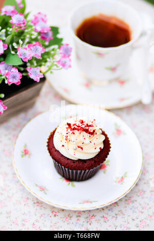 Ein roter Samt Kuchen mit Sahne serviert auf einem weißen, süßen rosa Blume Muster Platte zusammen mit Tee- Set Stockfoto