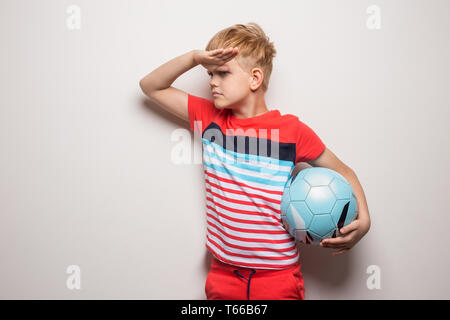 Süße kleine Junge stehend mit Fußball und Kamera. Auf weiß isoliert. Studio Portrait Stockfoto