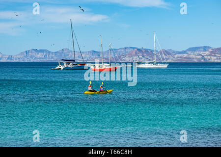 Ein paar Paddel gelb Kajak mit Segelbooten und die Berge im Hintergrund wie Vögel fliegen Overhead an der Küste der Isla San Francisco, Baja California S Stockfoto