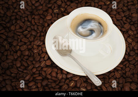 Tasse Kaffee mit Teelöffel auf Kaffeebohnen backgr Stockfoto
