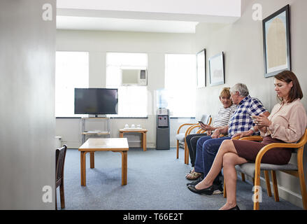 Patienten, die auf, unter Verwendung von Smart Phones in Klinik Wartezimmer Stockfoto