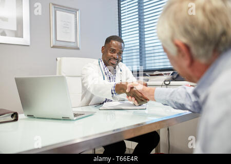 Männlicher Arzt Händeschütteln mit älteren Patienten in der Arztpraxis Stockfoto