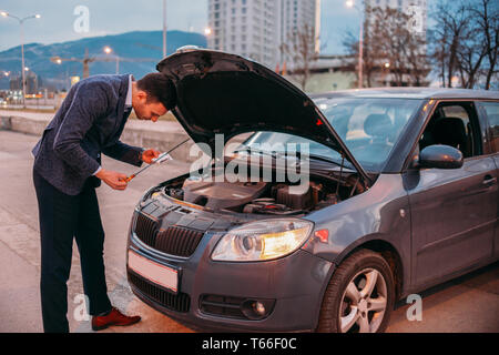 Einen müden Arbeiter steht neben seinem Auto formell gekleidet und Suchen über die Autos Motor Problem besorgt. Stockfoto