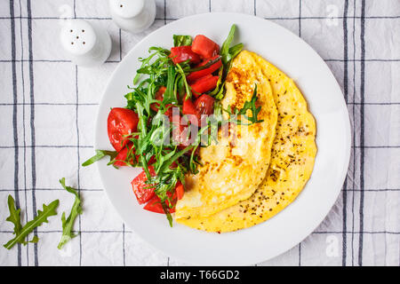 Klassische Omelett mit Käse und Tomaten Salat auf einem weißen Teller. Stockfoto