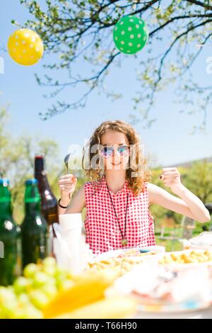 Jugendlich im Alter von Mädchen in rot kariertem Hemd sitzt von Tabelle auf Geburtstag Garten party-sonnigen Tag Stockfoto