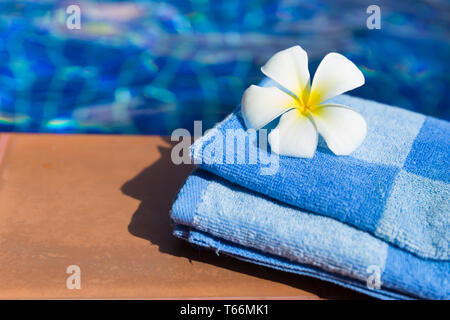 Flauschige blaue Handtuch mit plumeria frangipani Blume an der Grenze von einem Pool Stockfoto