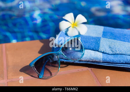 Flauschige Handtuch mit Sonnenbrille und Blume an der Grenze von einem Pool Stockfoto