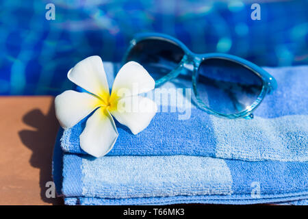 Flauschige Handtuch mit Sonnenbrille und Blume an der Grenze von einem Pool Stockfoto