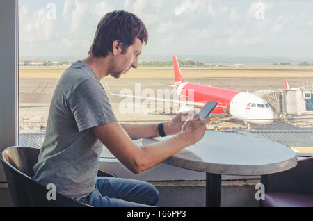 Junger Mann sein Handy einchecken am Flughafen. Auf dem Flug. Unternehmer im Airport mit dem Flugzeug im Hintergrund. Stockfoto