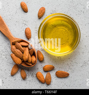 Mandelöl in Glas Schüssel und Löffel mit Mandeln auf konkreten Hintergrund, Ansicht von oben. Vegan fette Konzept Stockfoto