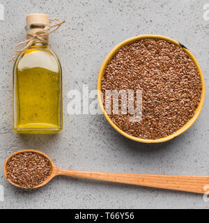 Leinöl in Flasche, Schüssel und Löffel Leinsamen auf konkreten Hintergrund, Ansicht von oben. Gesunde fette Konzept Stockfoto