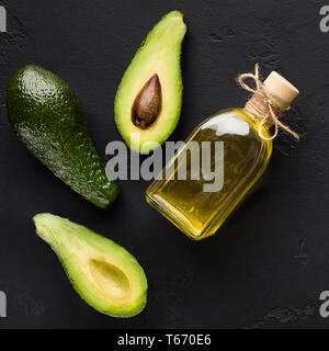 In Scheiben geschnitten und ganze Avocados und Öl in der Flasche auf dunklem Hintergrund der Ansicht von oben. Organische Öle Konzept Stockfoto