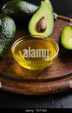 Avocadoöl in der Schüssel und frische Avocados auf Holzbrett. Stockfoto