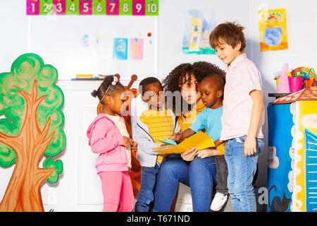 Gruppe von verschiedenen suchen Kinder Buch lesen mit Lehrer im Kindergarten Klasse Stockfoto