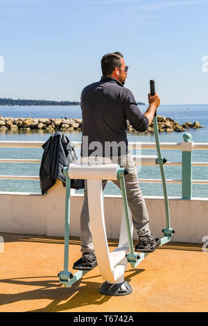CANNES, Frankreich - April 2019: Person mit einem Cross Training Maschine an ein Fitnessbereich im Freien an der Promenade in Cannes. Stockfoto