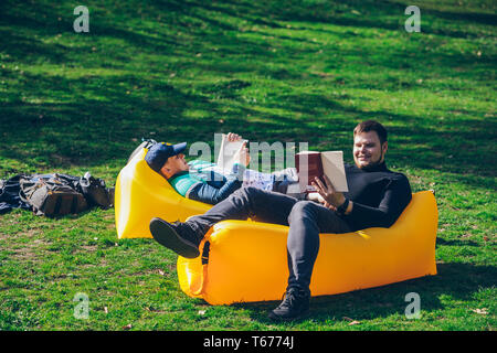 Zwei Männer Freunde Festlegung auf Gelb aufblasbare Matratze, Bücher zu lesen. sonniger Frühlingstag, Stockfoto