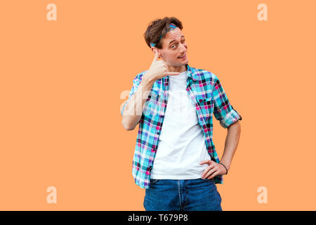 Portrait von lustigen jungen Mann im casual blau kariertem Hemd und Stirnband mit Anruf Geste die Hand in der Nähe der Ohren und die Pflege von Kamera mit einem Augenzwinkern. Stockfoto