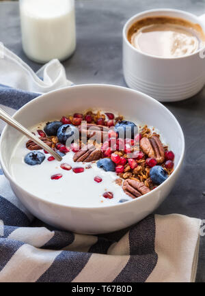 Hausgemachtes Müsli, Müsli mit Granatapfel Samen, Blaubeeren, Pekannuss und Joghurt auf grauem Beton Hintergrund. Gesundes Frühstück Schüssel. Stockfoto