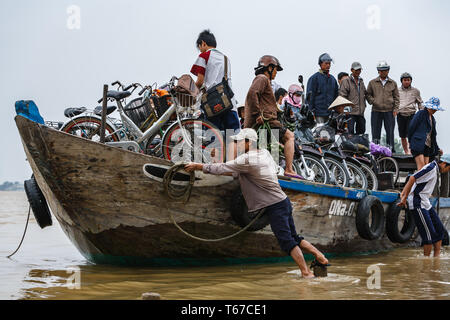 Mann zieht Boot Leute, die mit Lebensmitteln, Fahrräder, Schuhe, Motorräder auf Ufer in der Halong Bucht, also Sie können Stockfoto