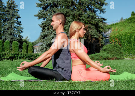 Junges Paar Üben Yoga im Freien im Park auf Matte zurück zu sitzen zurück Meditation lächelt glücklich Stockfoto