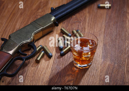 Wild West Gewehr und Munition mit Glas mit Whiskey und Eis auf Bar aus Holz Tisch Stockfoto