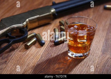 Wild West Gewehr und Munition mit Glas mit Whiskey und Eis auf Bar aus Holz Tisch Stockfoto