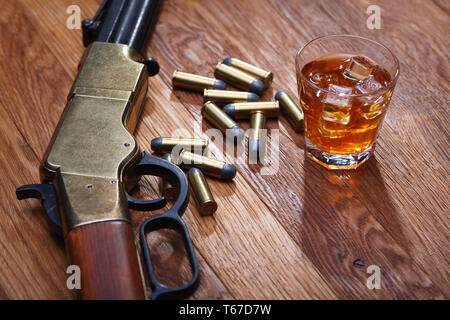 Wild West Gewehr und Munition mit Glas mit Whiskey und Eis auf Bar aus Holz Tisch Stockfoto