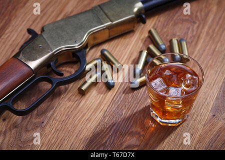 Wild West Gewehr und Munition mit Glas mit Whiskey und Eis auf Bar aus Holz Tisch Stockfoto