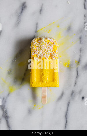 Blick von oben auf die hausgemachte Eiscreme aus Kokosmilch und Gefrorenes Mango über weißen Marmor. Gesunde veganes Essen und Sommer Konzept. Stockfoto