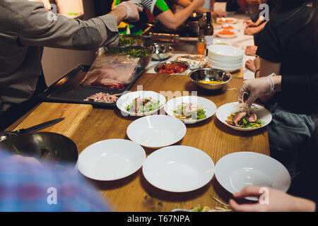 Ein männlicher Chef schmückt ein Salat Gericht in einem Restaurant Küche in einer schwarzen Schürze. Nahaufnahme einer Hand mit der Zange. Stockfoto